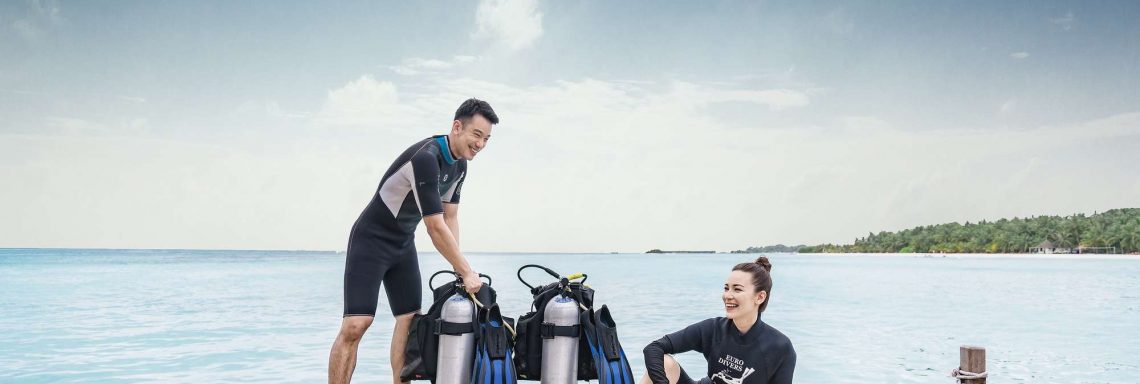 Club Med Villas of FInolhu, Maldives - Photo of two smiling people preparing to dive in front of the ocean with carboys