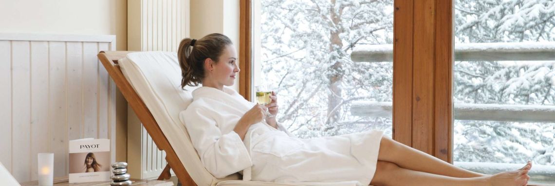 Club Med Serre-Chevalier, in France - Image of a woman in a bathrobe lying on an indoor deckchair with a view of the snowy landscape  