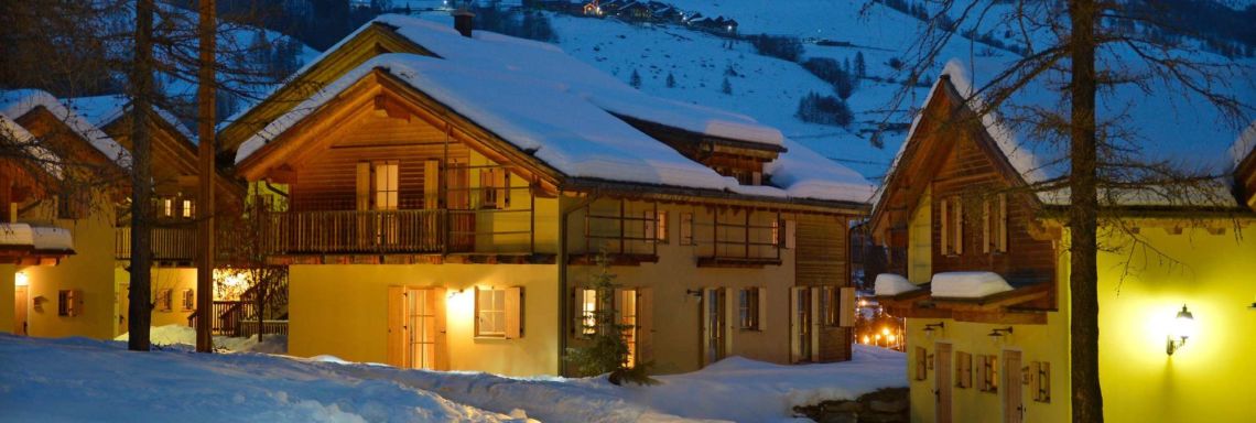 Club Med Pragelato Vialattea, Italy - Small, two-storey chalets lit up in the evening.
